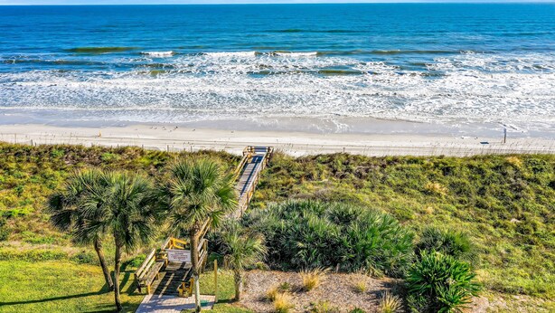 A coastal view with a beach, ocean, and a pathway leading to a boardwalk with benches. - Oceanfront condo with pool, ocean views, and washer/dryer (St. Augustine)