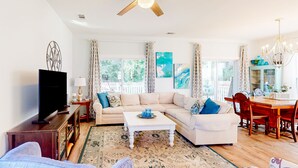 A living room with a sofa, coffee table, TV, and dining area with chairs and a chandelier. - Charming home steps from the beach with enclosed yard and grill - dog-friendly (St. Augustine)