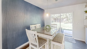 A dining area with a glass-top table, white chairs, and a blue accent wall.