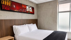 A modern bedroom with a bed, a wooden nightstand, a large abstract painting, and a window. - Best bang for your buck in Laureles (Medellín)