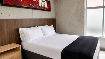 A modern bedroom with a bed, a wooden nightstand, a large abstract painting, and a window.