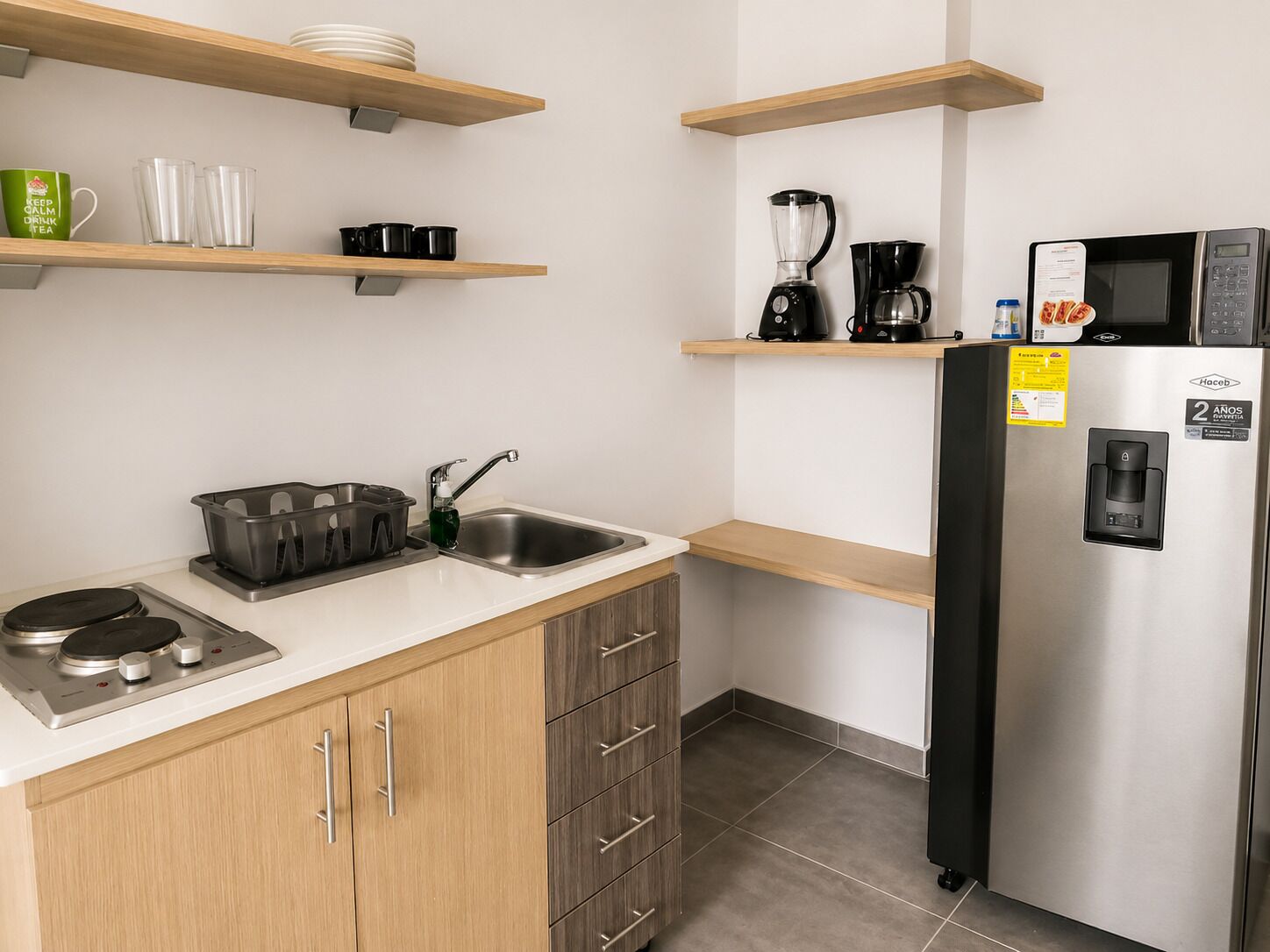 A modern kitchen with wooden cabinets, a stainless steel sink, a coffee maker, a blender, and a refrigerator.
