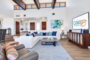 A spacious living room with a white sofa, a coffee table, and a leather couch. There is a wooden cabinet and a painting on the wall.