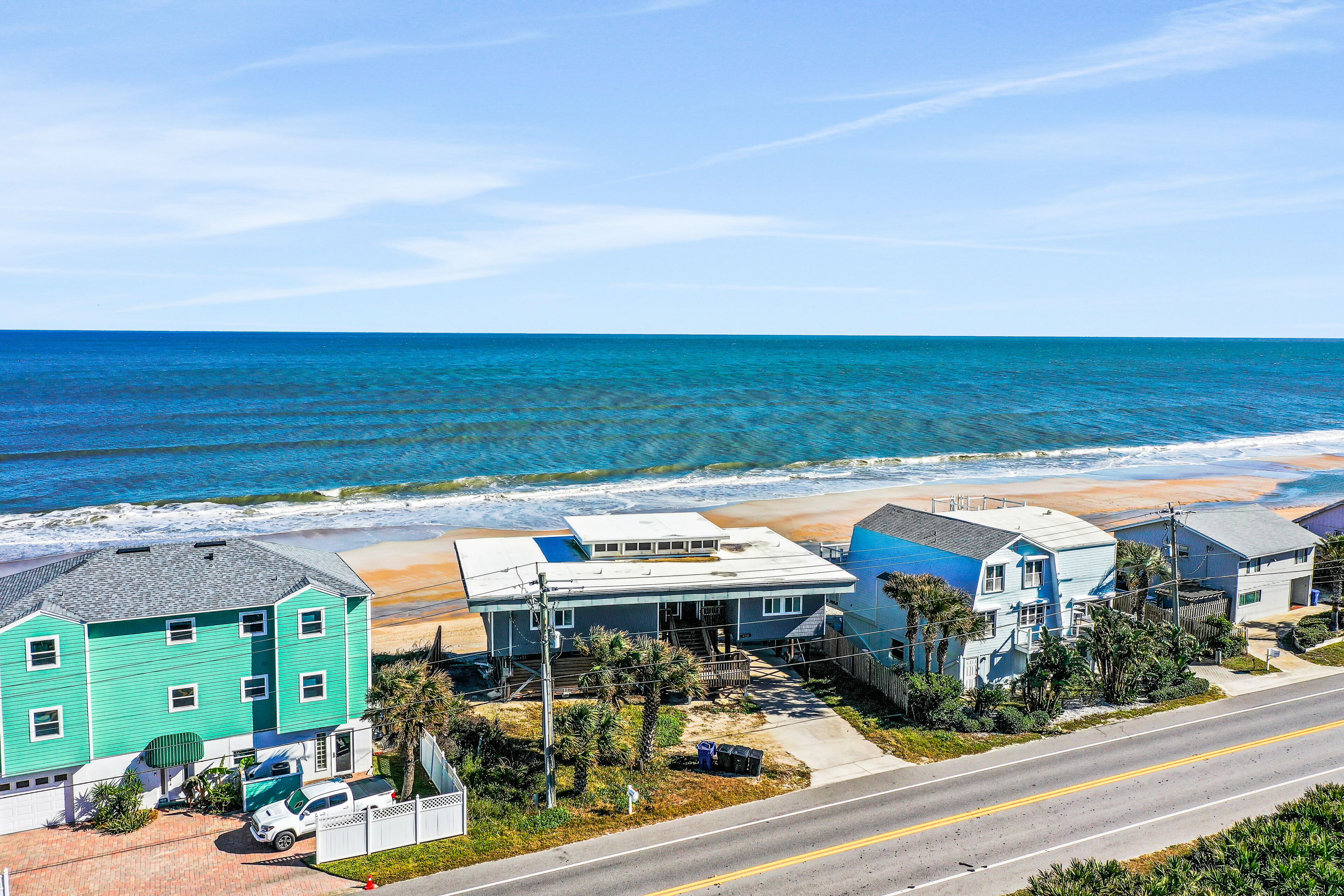 A coastal residential area with houses near the beach, a clear road, and the ocean in the background.
