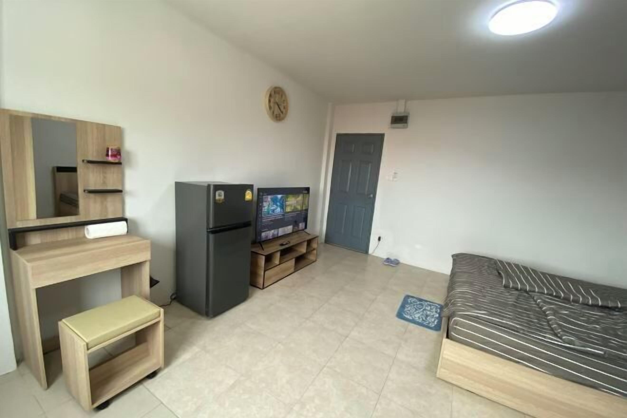 Ett kompakt bostadsutrymme med en säng, ett litet skrivbord med en stol, en tv och ett kylskåp.