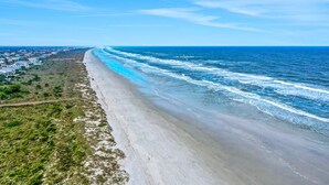 Ein Küstenstrand mit einer weiten Sandküste, einer parallel zum Strand verlaufenden Straße und einer entfernten Ansicht einer Stadt.
