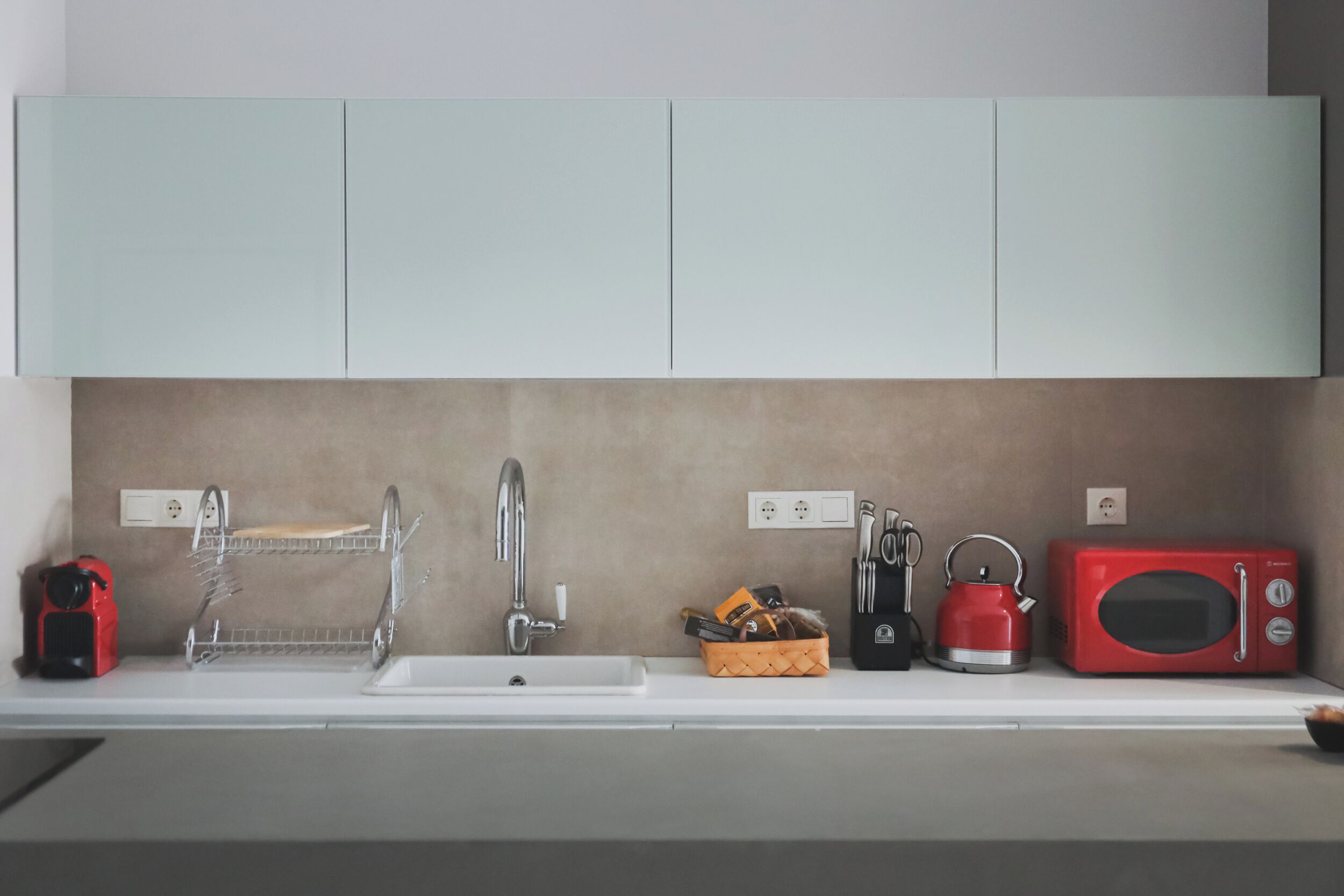 Een moderne keuken met een wit aanrecht, een rode waterkoker, een rode magnetron en een messenblok.