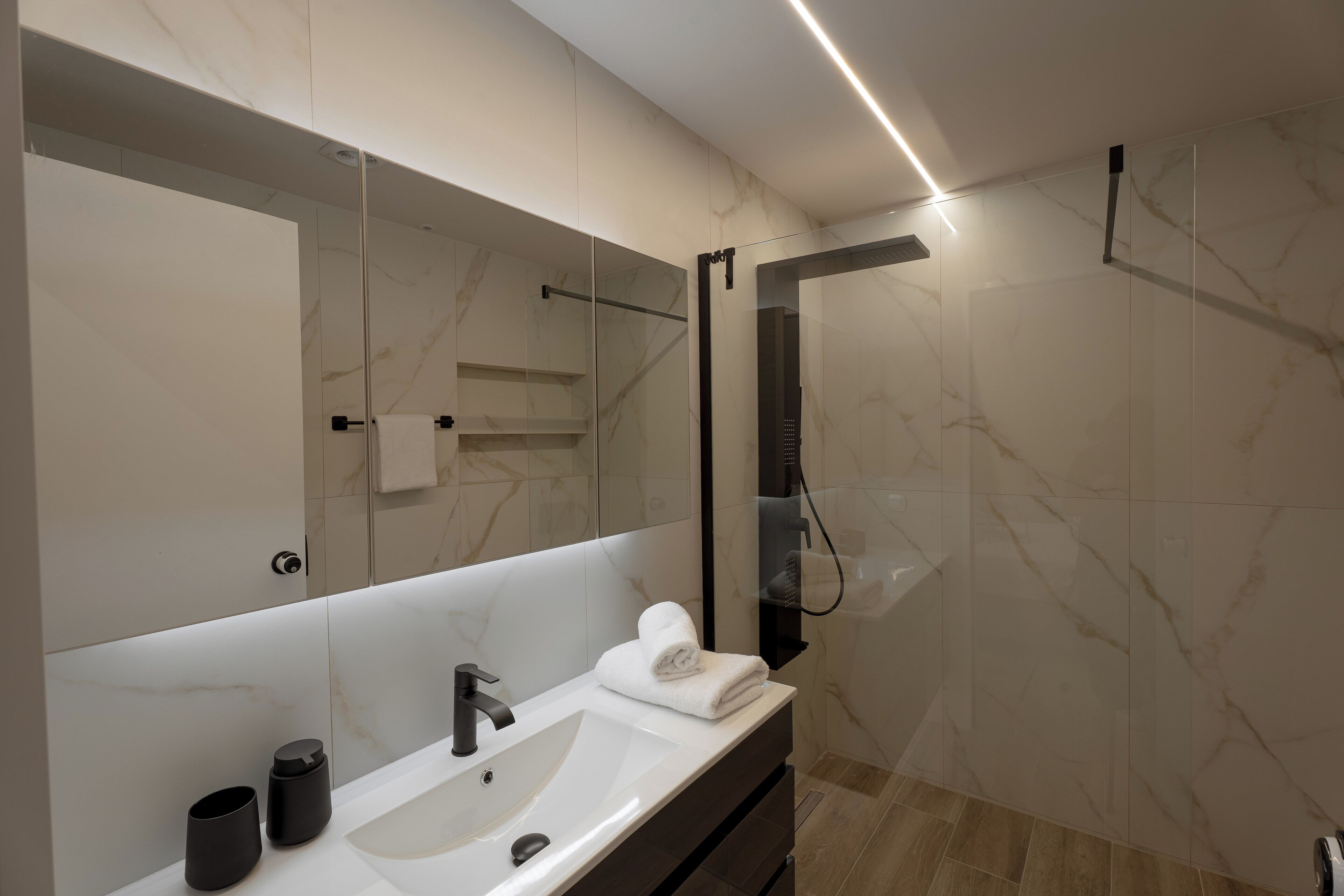 Un baño moderno con un espejo grande, un lavamanos y una ducha.