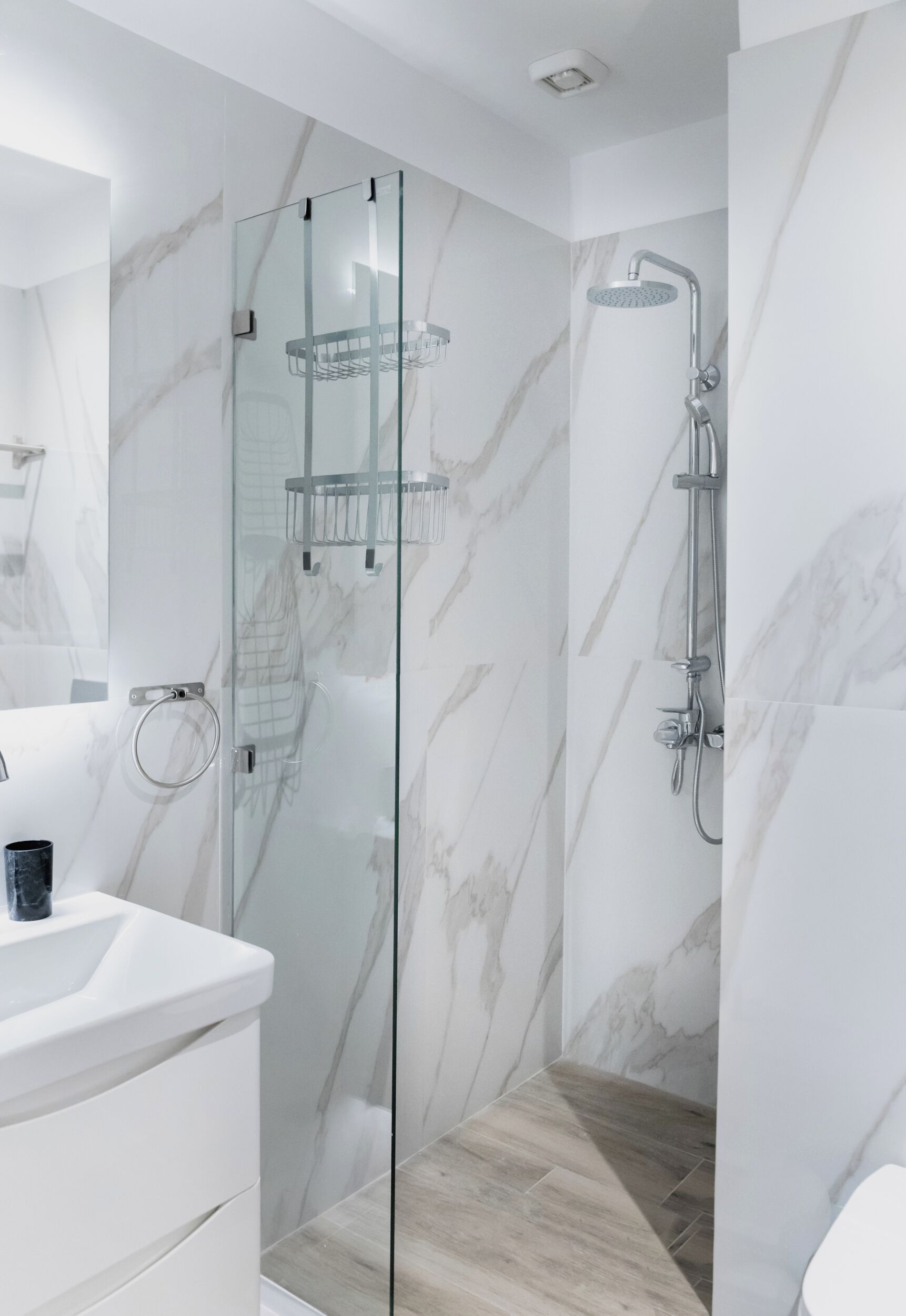 Une salle de bain moderne avec une douche à parois de verre, des murs en marbre et un plancher en bois.