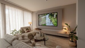 A modern living room with a large flat-screen TV mounted on the wall, a comfortable sofa set, a glass coffee table, and a potted plant. - Athens Soho Lofts - Evagelistrias Pedestrian (Athens)