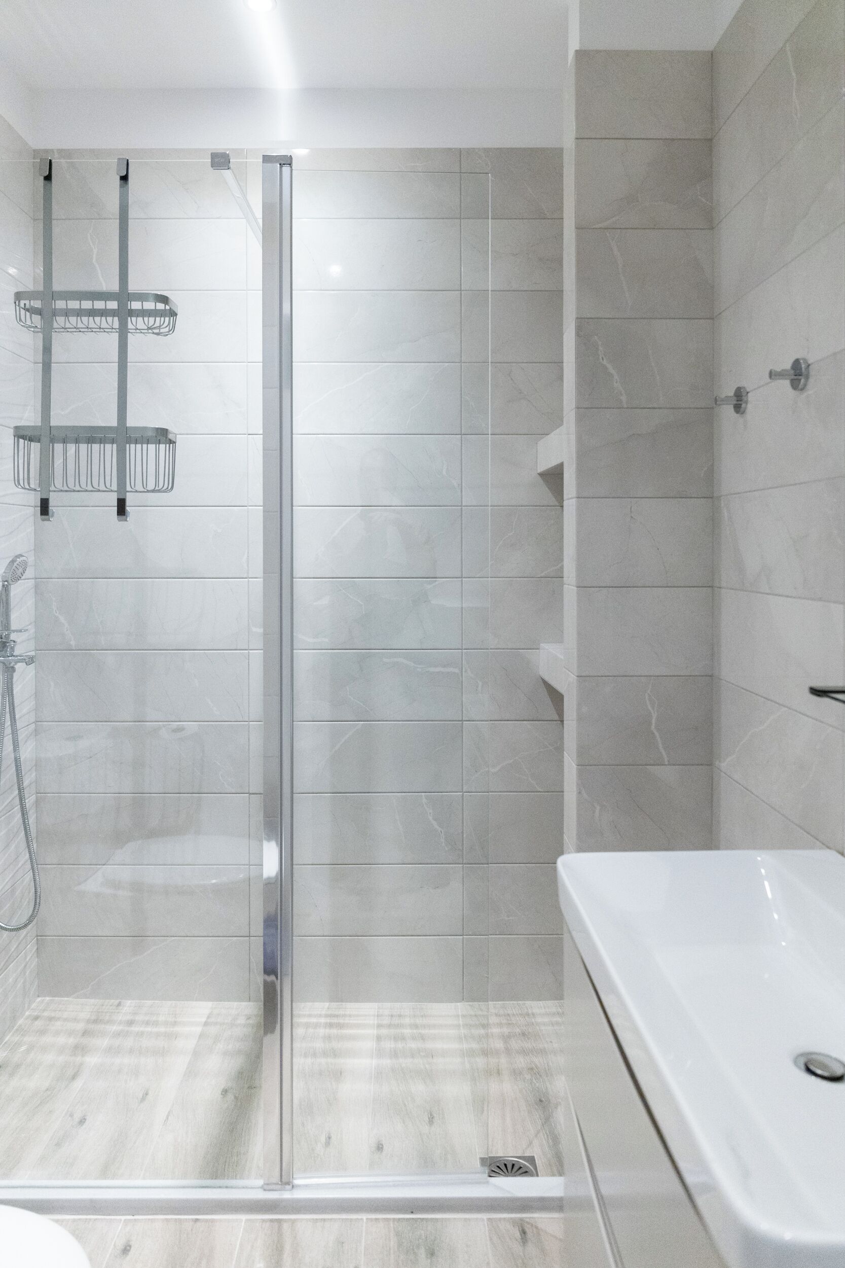 A modern bathroom with a glass-enclosed shower, a white bathtub, and a tiled floor.