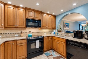 A modern kitchen with wooden cabinets, a black stove, a microwave, and a coffee maker.