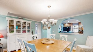 Un coin repas comprenant une table en bois, des chaises blanches, un lustre et un buffet aux portes vitrées.