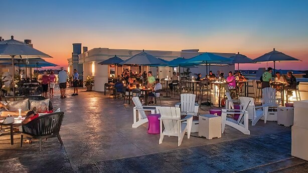 An outdoor seating area with tables and chairs, umbrellas, and a view of the sunset. - Lower Level 1 Block from 2 Beaches w/Private Pool, High-Speed Wi-Fi (St. Augustine)