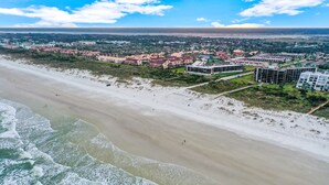 Luchtbeeld van een kustgebied met een strand, gebouwen en een verre kustlijn.