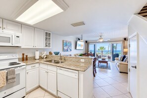 A modern kitchen with white cabinetry, a granite countertop, and a view to a balcony with outdoor furniture.