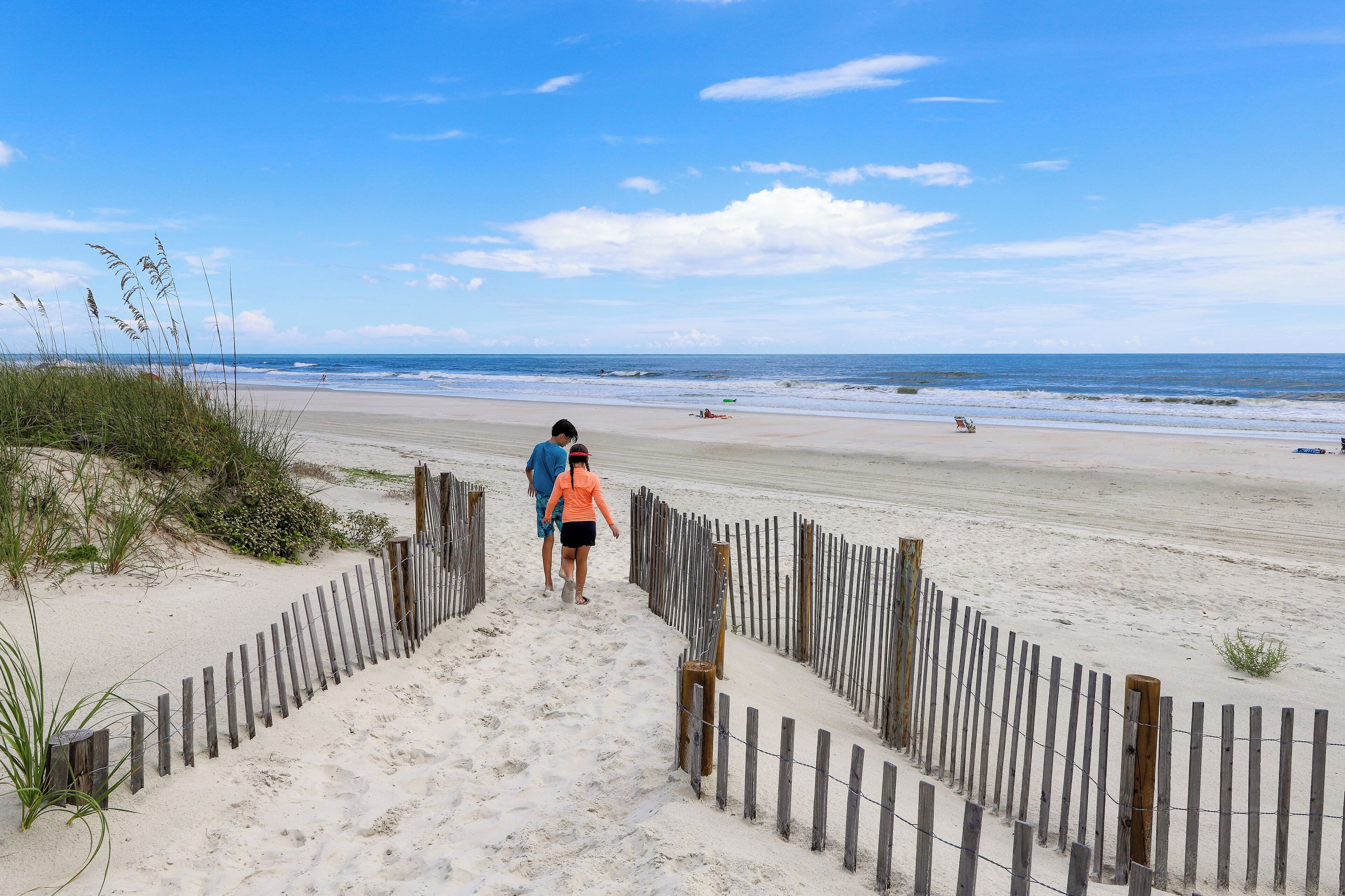 A sandy beach with a wooden fence leading to the water.