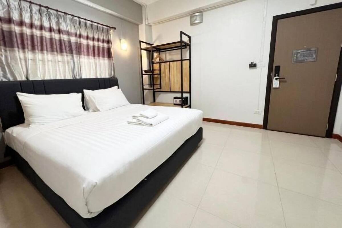 A hotel room with a large bed, a wardrobe, a door with a sign, and a window with curtains.