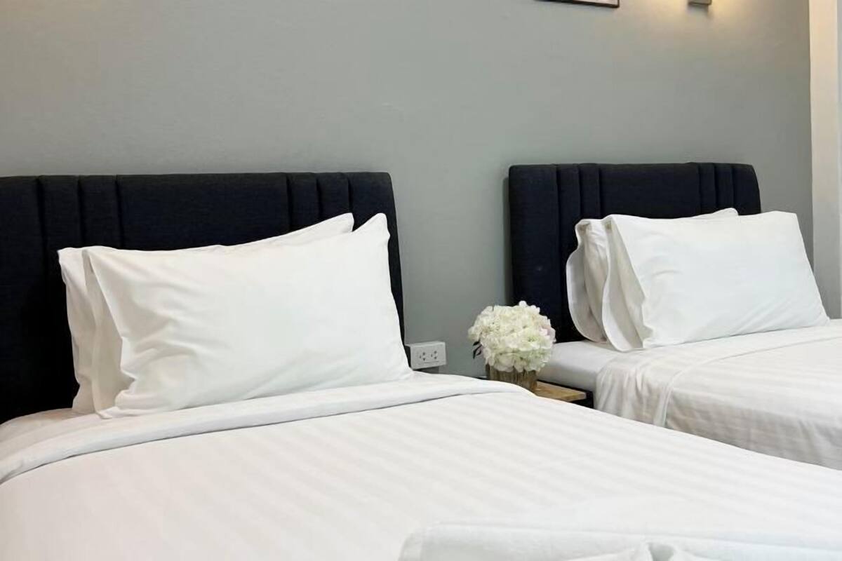 Two adjacent beds with dark headboards, white bedding, and a small vase with white flowers on a nightstand.