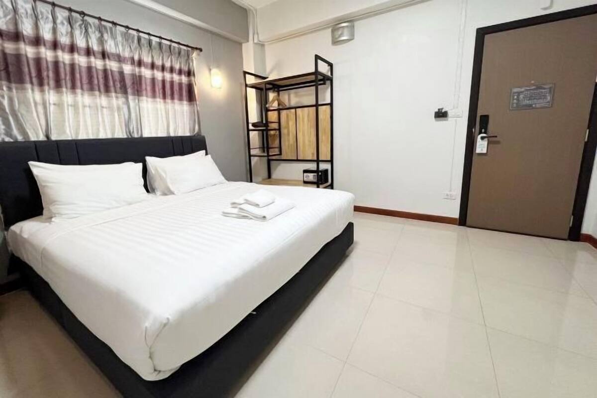 A hotel room with a bed, a wooden shelf unit, a door, and a curtain.