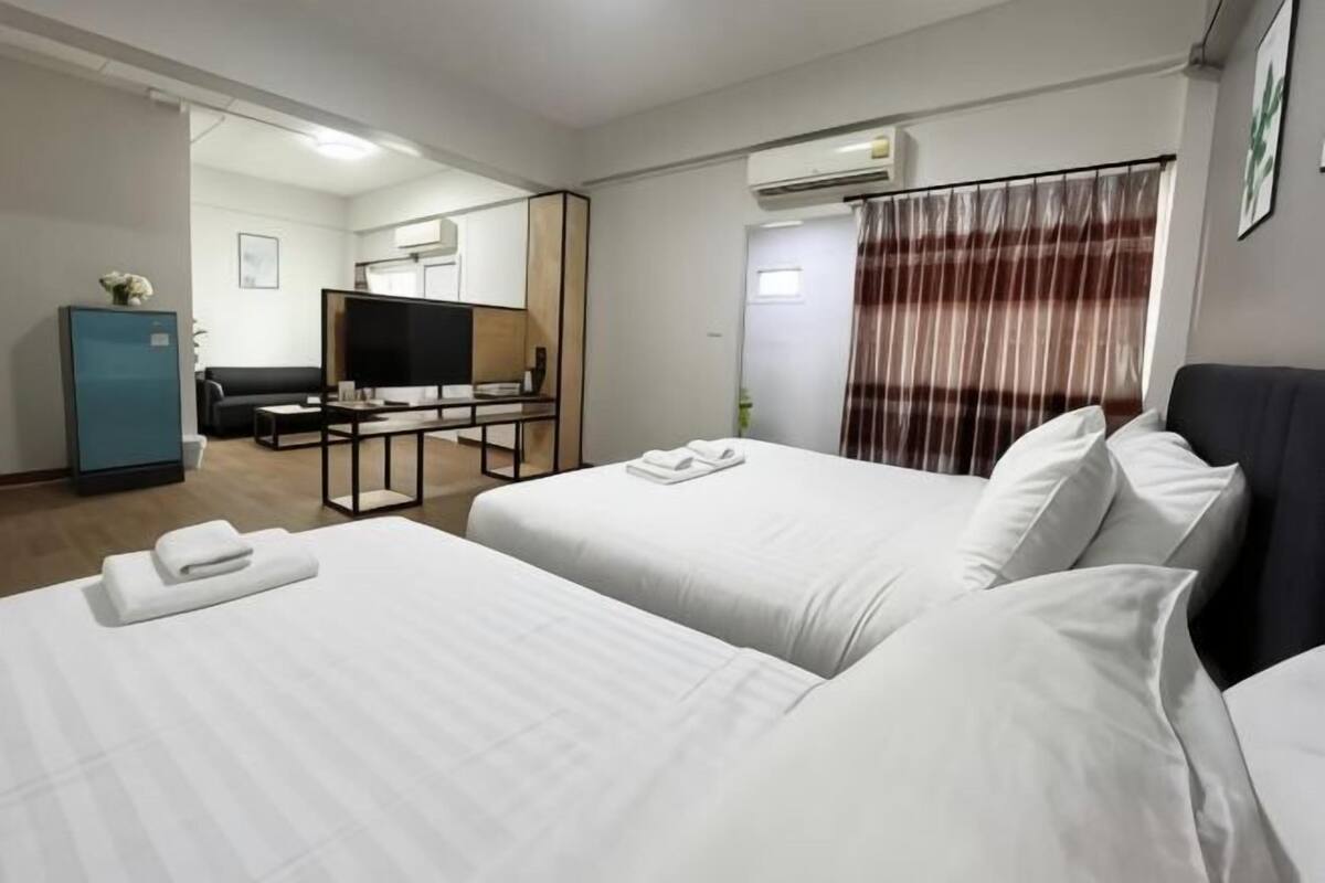 A hotel room with two beds, a desk with a television, a wardrobe, and an air conditioning unit.