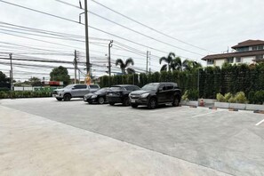 A parking lot with several cars parked, a building in the background, and a hedge along the side. - Golden Nest Hotel Suvarnabhumi (Bangkok)
