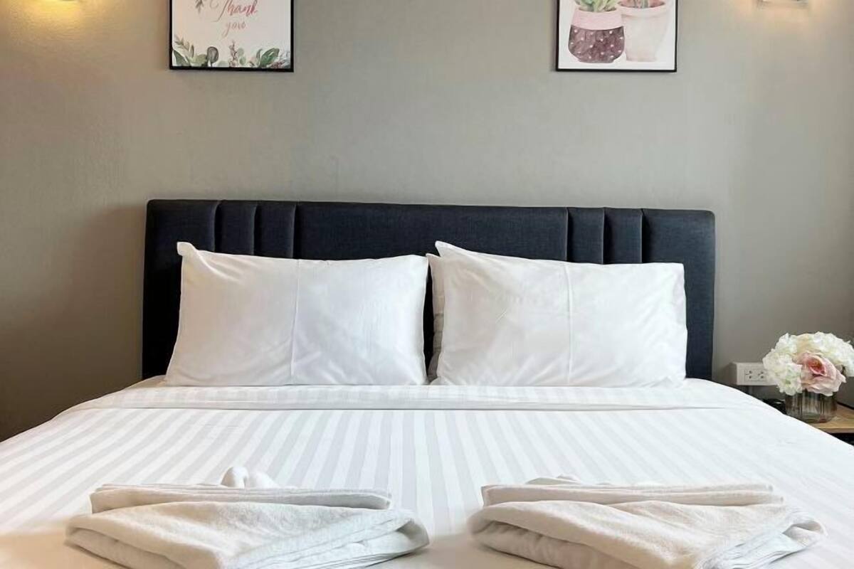A neatly made bed with white pillows and striped bedding, a dark headboard, and a small vase with flowers on the nightstand.