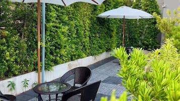 An outdoor seating area with a table and chairs, surrounded by a hedge and an umbrella.