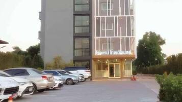 A building with a modern facade, a parking lot with several cars, and a sign that reads 'Hotel'.
