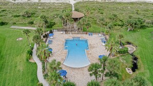 Luftaufnahme eines Resorts mit einem zentral gelegenen Swimmingpool, umgeben von Palmen und einem Strandweg.