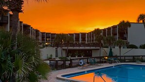 A swimming pool with lounge chairs and palm trees, surrounded by a building with balconies. - Oceanview condo with beach access, pool, tennis courts and private patio (St. Augustine)