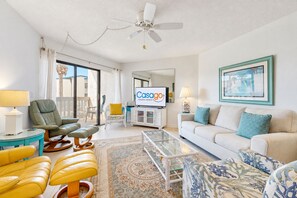A well-lit living room with a television, seating area, and a view to the outside.