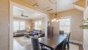 A spacious living room with a large wooden dining table, leather sofas, and a ceiling fan. - Pet -Friendly Home Walking Distance to Down St Augustine (St. Augustine)