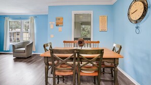 A dining room with a wooden table and chairs, a chandelier, and a clock on the wall. - Charming Condo w/ Pool – 500 Yards to Beach, Near Lighthouse & Downtown (St. Augustine)