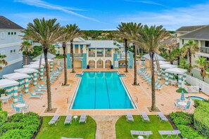 A swimming pool with lounge chairs and umbrellas, surrounded by palm trees and a building with a light blue and white facade. - Oceanview condo with resort amenities, balcony and private beach access (Palm Coast)