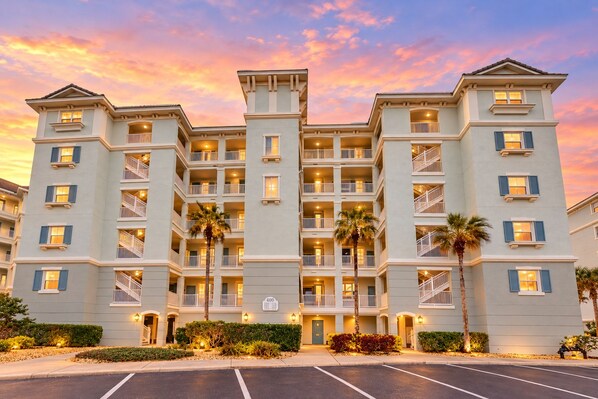 A multi-story hotel with balconies, a parking lot, and a sunset sky. - Oceanview condo with resort amenities, balcony and private beach access (Palm Coast)
