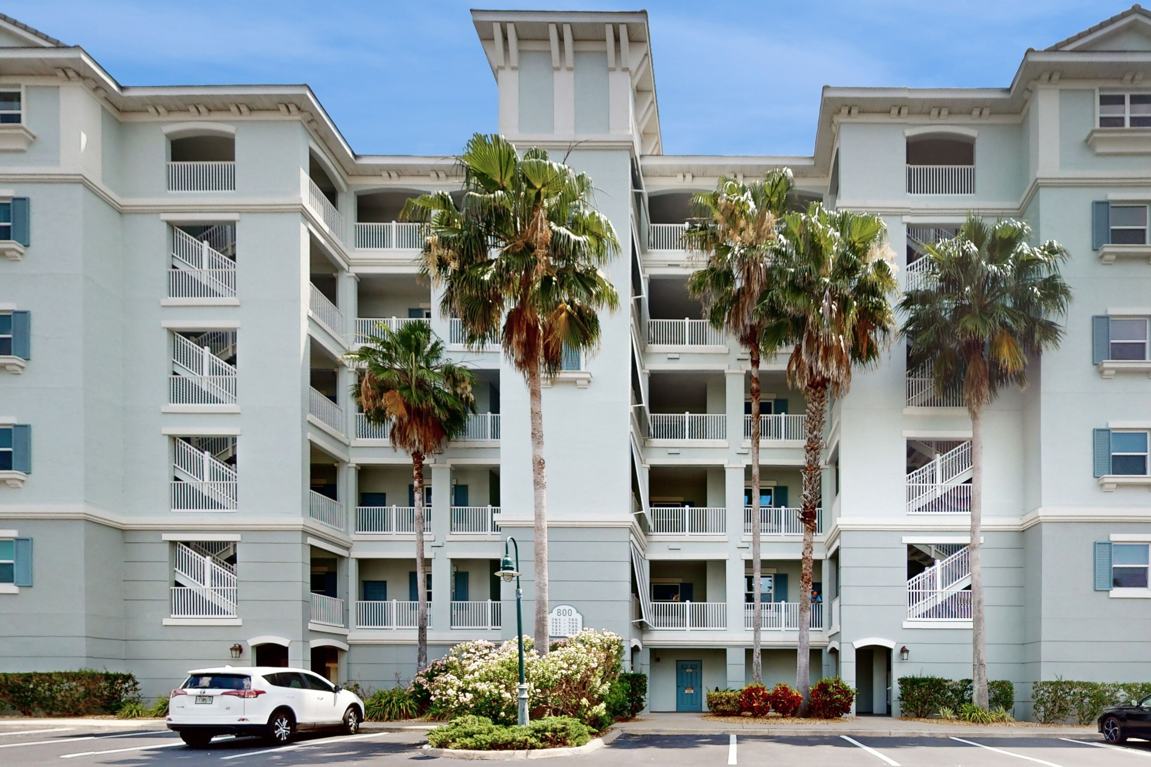 A multi-story hotel with balconies, palm trees, and a parking lot.