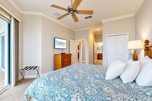 A bedroom with a bed, a ceiling fan, a TV, a dresser, and a bathroom visible through an open door. - Oceanview condo with resort amenities, balcony and private beach access (Palm Coast)