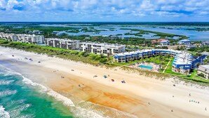 An aerial view of a beachfront hotel with multiple buildings, a sandy beach, and a clear view of the ocean. - Island-themed living with furnished patio, shared pool & beach access (St. Augustine)