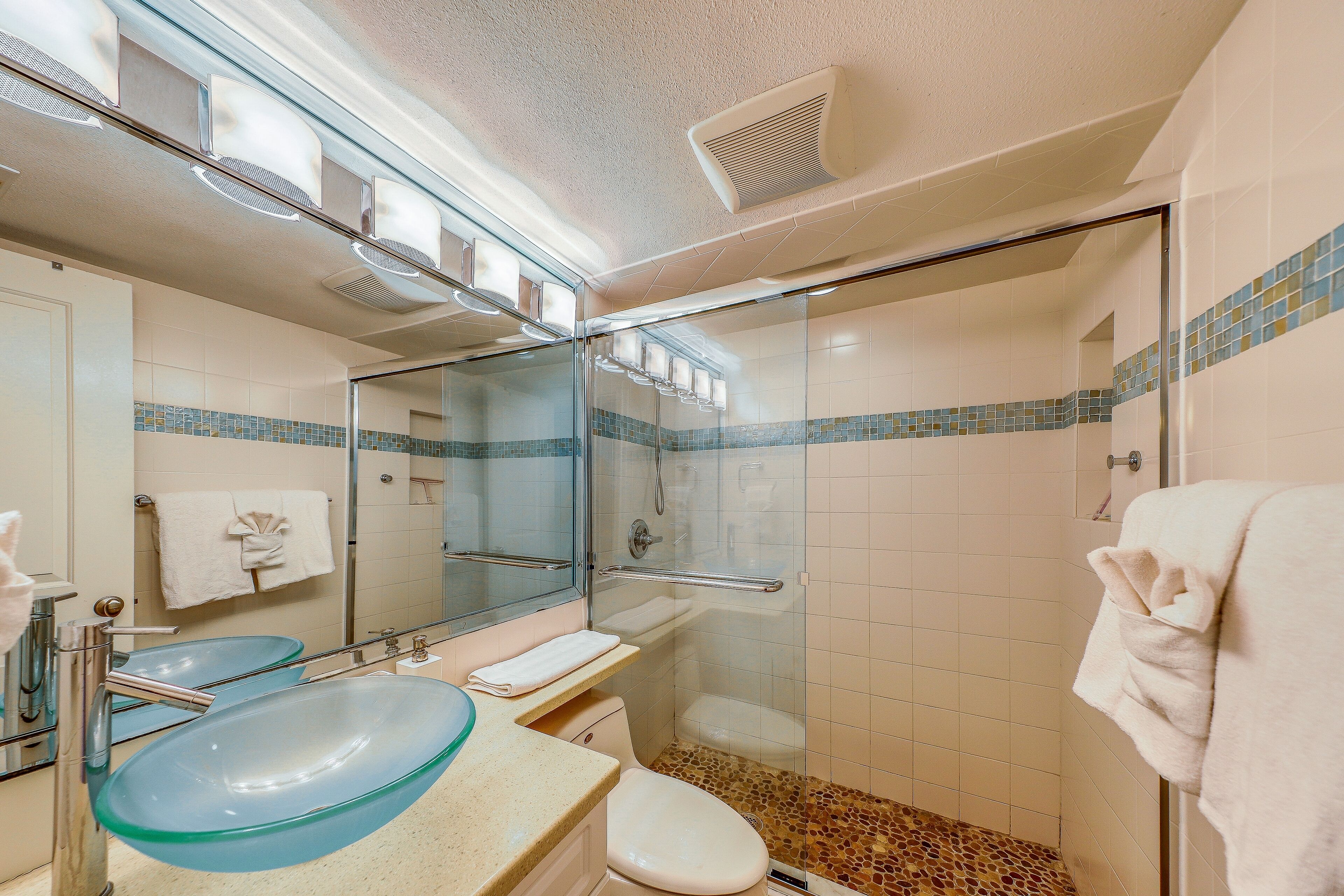 Une salle de bain moderne dotée d’une douche à parois de verre, d’un lavabo double avec un récipient en verre bleu et de toilettes blanches.