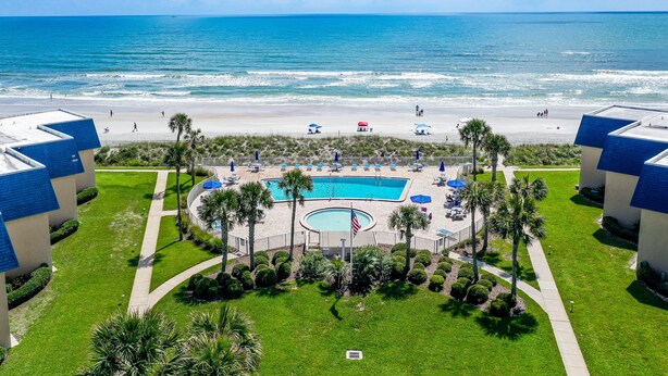 A resort with a swimming pool surrounded by palm trees and a beach view. - Island-themed living with furnished patio, shared pool & beach access (St. Augustine)