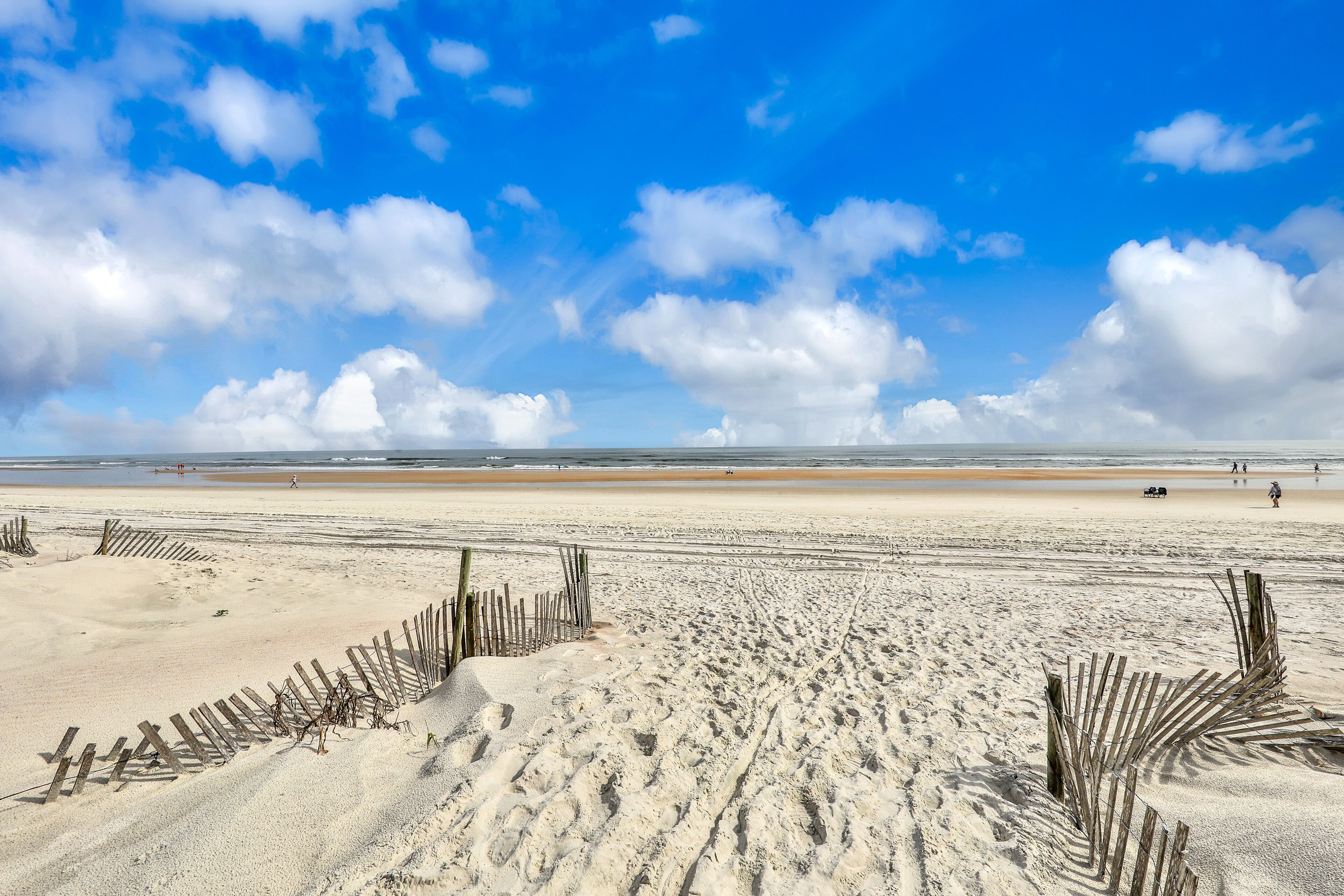 A wide sandy beach with wooden barriers and a clear blue sky.