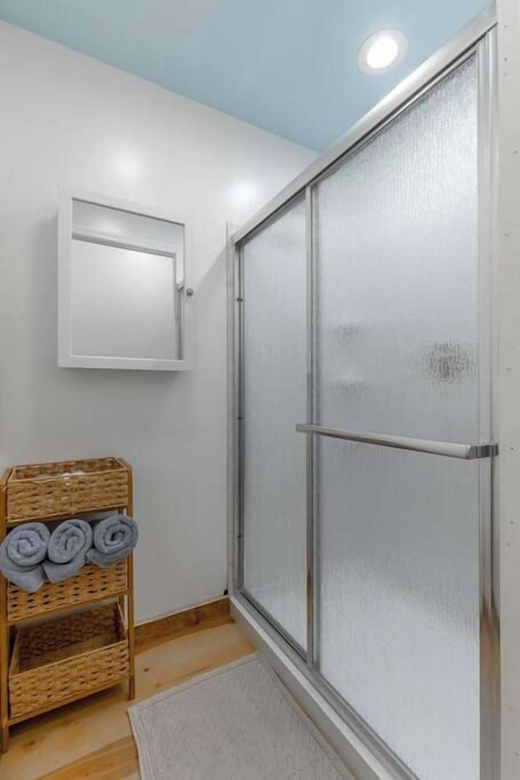 Una ducha con puertas de vidrio satinado, una pared blanca y un piso de madera.