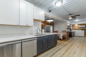 A modern kitchen with white cabinets, a built-in dishwasher, and a dining area with a wooden table and chairs. - Mountain Container Treehouse Lookout Mtn (Lookout Mountain)