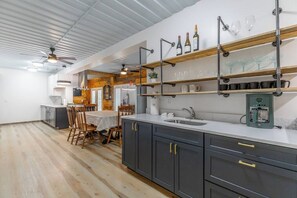 A modern kitchen with dark cabinets, a white countertop, and a dining area with wooden chairs.