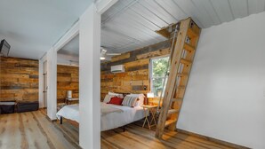 Ein Schlafzimmer mit schrägen Wänden, Holzboden und -vertäfelung, einem Bett, einem Nachttisch und einer Leiter.