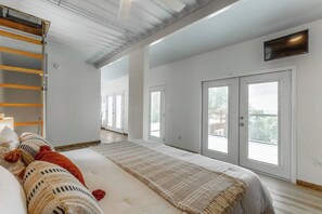 A spacious room with a large bed, a wooden ladder, and a view through glass doors.