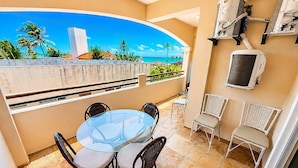 A balcony with a glass table and wicker chairs, overlooking a coastal view with palm trees and a clear sky. - Hosts BR - Vista Mar no Cumbuco  (Caucaia)