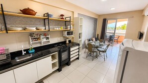 A modern kitchen with a gas stove, microwave, and dining area with a table and chairs. - Hosts BR - Vista Mar no Cumbuco  (Caucaia)