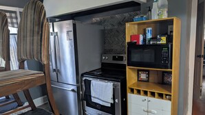 A compact kitchen with a refrigerator, oven, microwave, and a wooden cabinet with storage. - Step into this spacious-style home (Milwaukee)